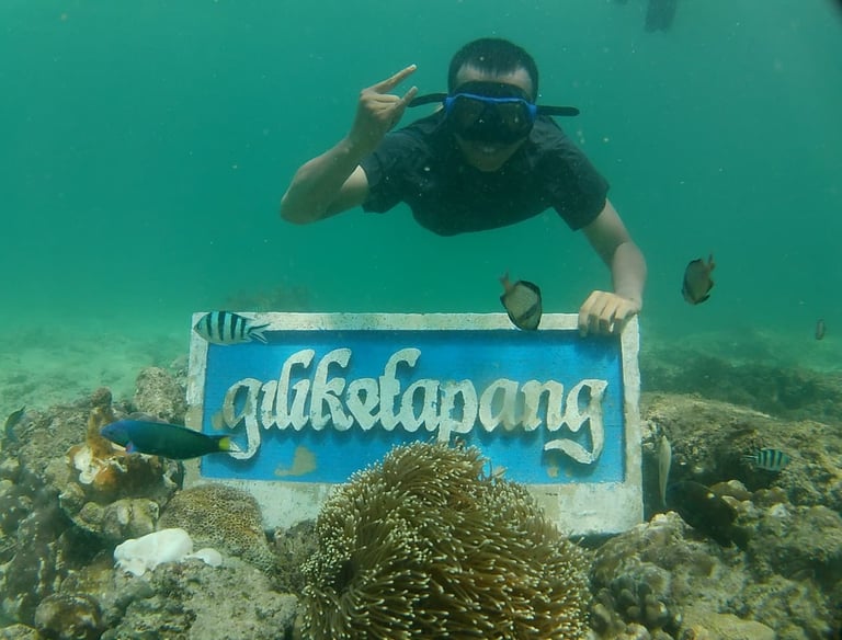 foto seorang pria menyelam atau snorkeling dan berpose di papan batu Gili Ketapang