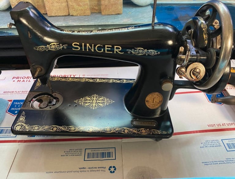 Vintage black Singer sewing machine with gold floral decals resting on a USPS Priority Mail box.