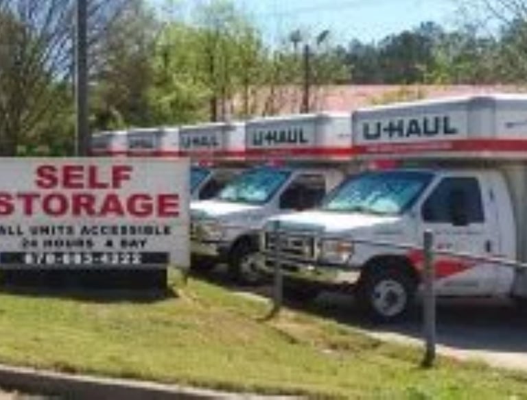 A row of U-Haul moving trucks parked at a self storage facility with a 24-hour access sign.
