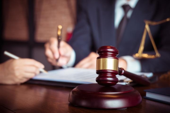 Professional lawyer in a suit signing legal documents next to a wooden judge gavel and scales of justice.