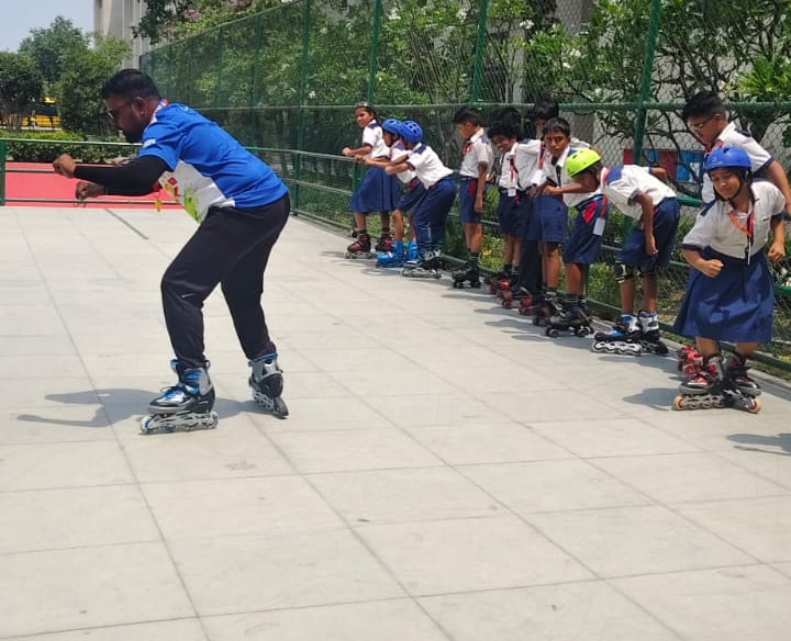 A group of school students in uniform with helmets learning inline skating from an instructor on an outdoor rink.