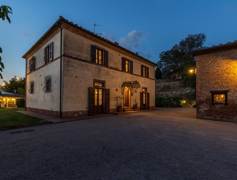 A historic luxury villa in Tuscany at twilight with illuminated windows and stone architecture.