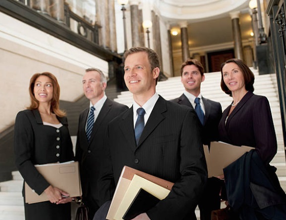 Professional lawyers and business executives in formal suits standing in a corporate building lobby.