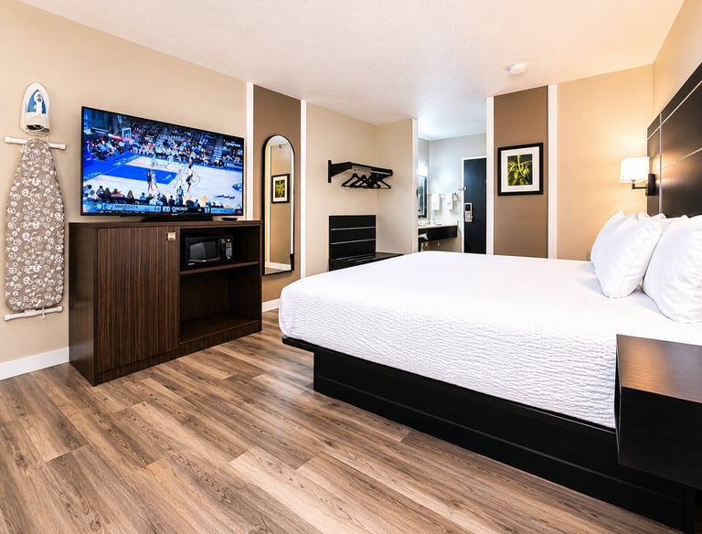 Modern hotel room featuring a king-sized bed, hardwood floors, and a flat-screen TV playing basketball