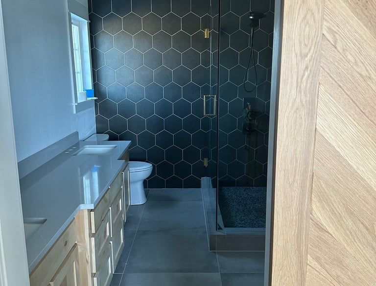 Modern bathroom featuring black hexagon wall tiles, a glass walk-in shower, and a light wood vanity.