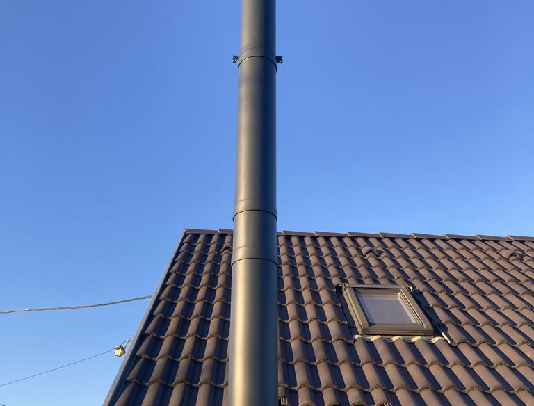 Családi ház barna cseréppel fedett tetején antracit színű, korrózióálló acélból készült kémény.