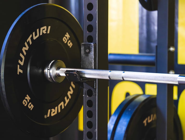 A barbell with a 5kg Tunturi bumper plate resting on a black steel power rack in a gym.