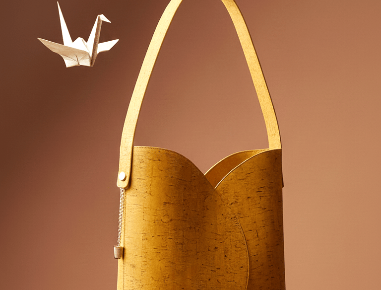 Eco-friendly yellow cork leather shoulder bag floating next to a white origami crane.