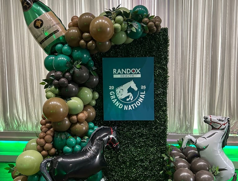 An elaborate Grand National event display features a large champagne bottle balloon, horse balloons, and a "RandoX Grand