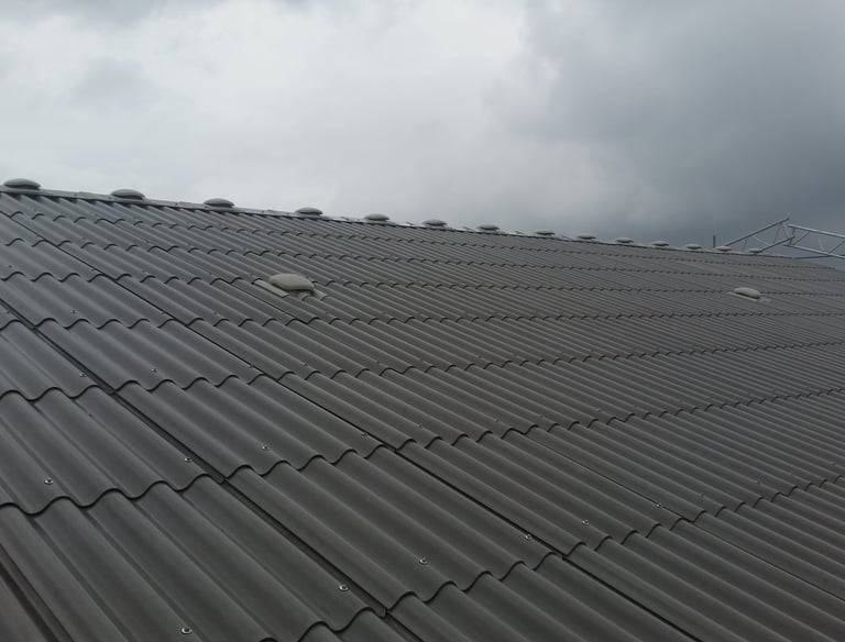 Holdbare grå tagplader i bølgeformet metal monteret på en erhvervsbygning under en overskyet himmel.