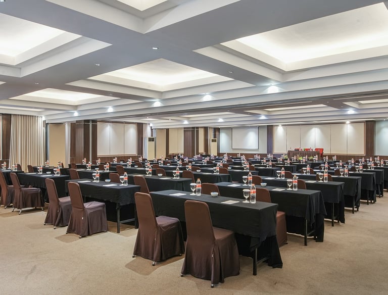 Spacious hotel conference room with rows of tables, brown chairs, and modern recessed lighting.