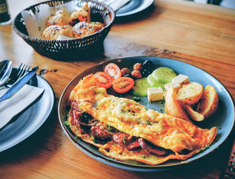Breakfast plate with a cheese omelette, roasted potatoes, tomatoes, and cucumber slices.
