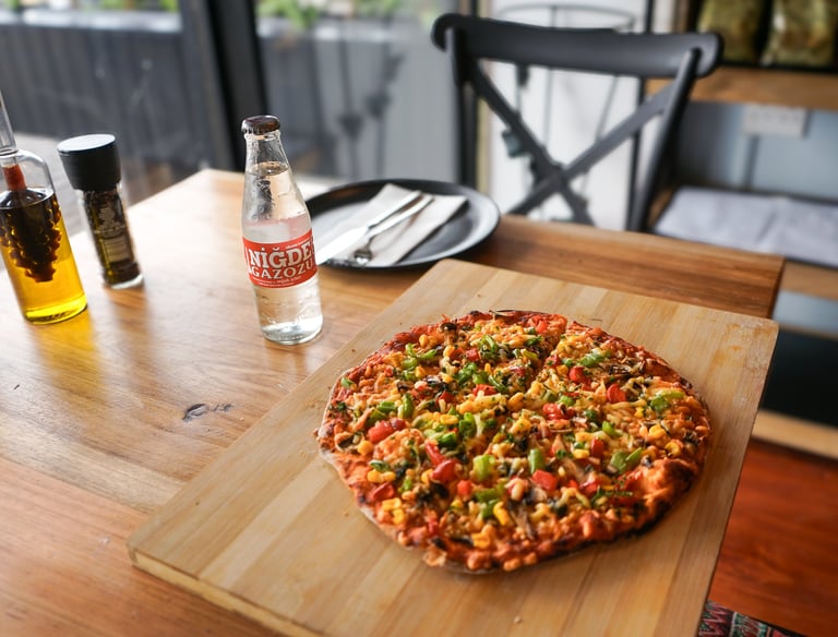Fresh vegetarian pizza with peppers and corn served on a wooden board next to a cold soda bottle.