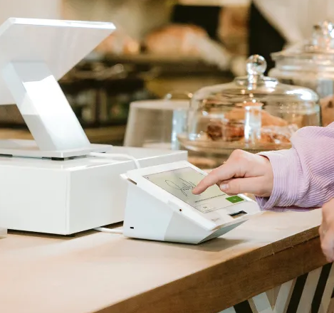 Customer using a touchscreen POS terminal to sign for a digital payment at a cafe counter.