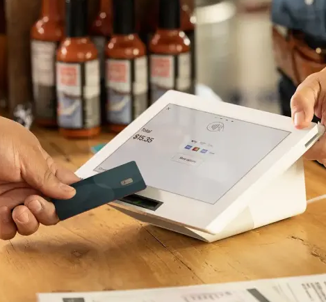 Customer paying with a credit card at a white touchscreen point of sale terminal in a shop.