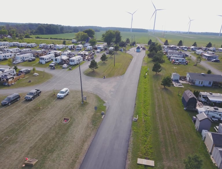 Aerial view of a spacious RV park and campground featuring paved roads, trailers, and wind turbines.
