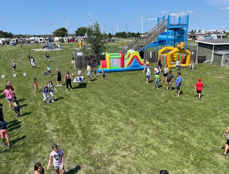 Families enjoy a summer festival at an RV park with inflatable bounce houses and a water slide.