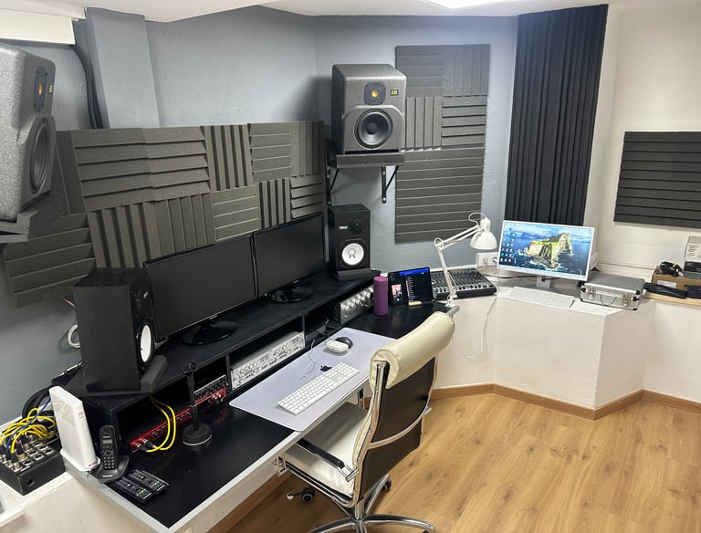 a recording studio with a computer monitor, speakers, and a laptop