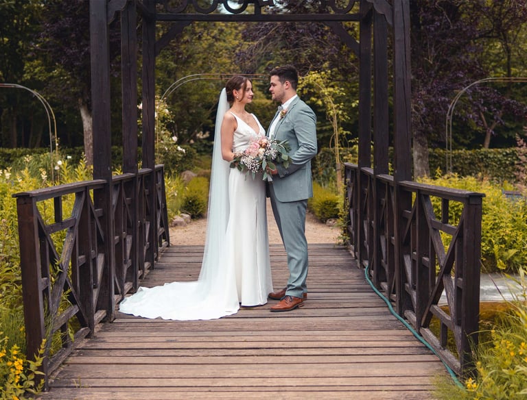 Brautpaar steht verliebt auf einer Holzbrücke im Grünen. Romantische Hochzeitsfotografie von Just Perspectives.
