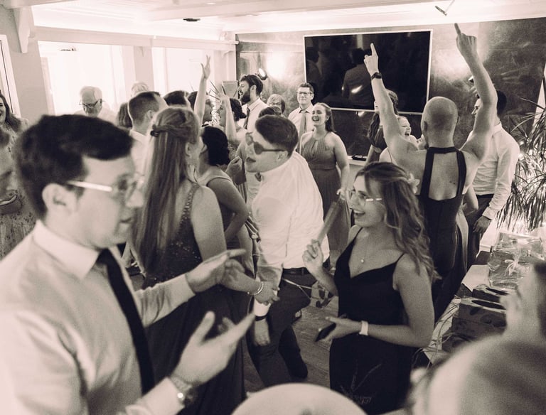 Ausgelassene Partygäste tanzen mit erhobenen Händen auf einer Hochzeitsfeier. Schwarz-Weiß-Foto von Joel Pingel.