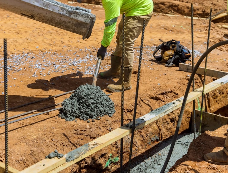 a man in a yellow jacket is pouring concrete into a concrete slab