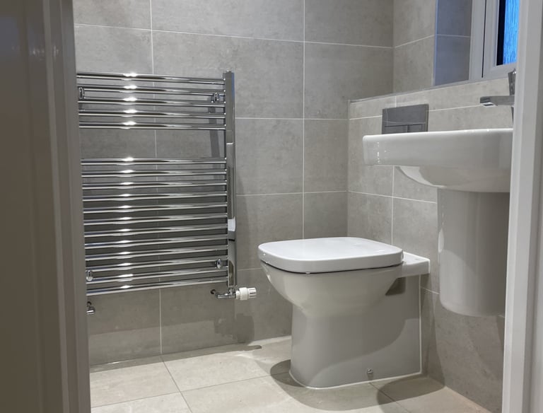 Modern bathroom with grey tiles, a white toilet, pedestal sink, and chrome heated towel rail.