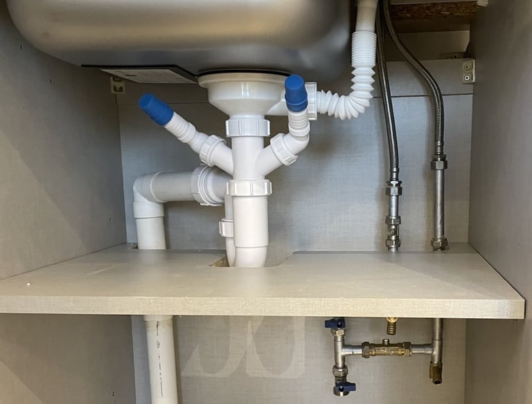 kitchen plumbing with a stainless steel sink drain, waste pipes, and flexible water supply pipes.
