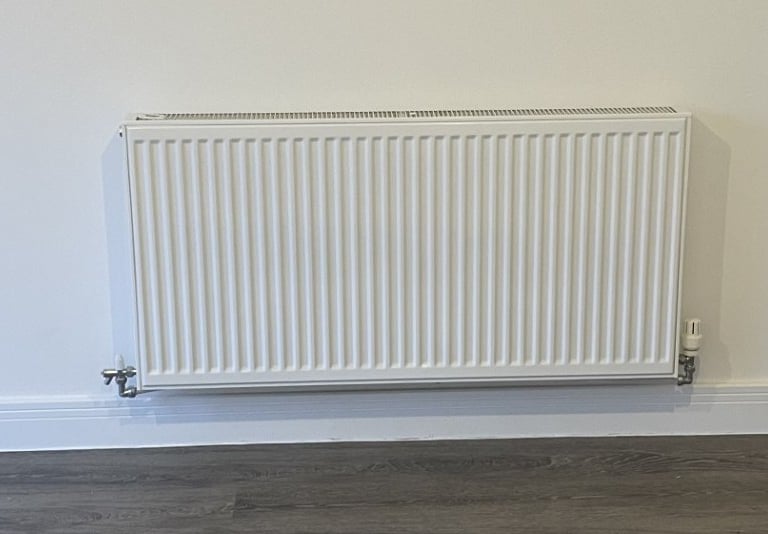 A modern white wall-mounted central heating radiator with a thermostat valve on a neutral wall.