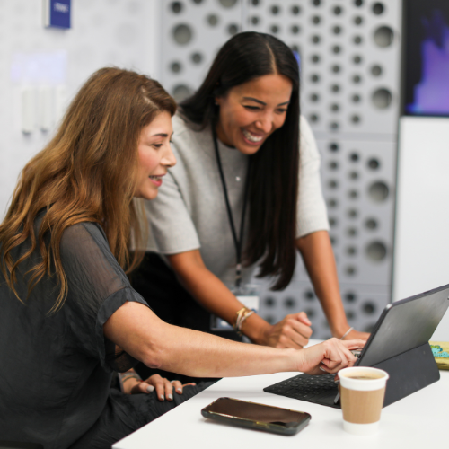 two women sitting at a table using an AI tool on a laptop