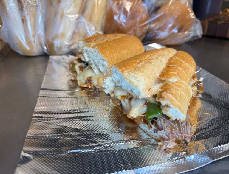 Texas-style brisket sandwich stacked with sautéed green peppers, onions, melted cheese, and drizzled