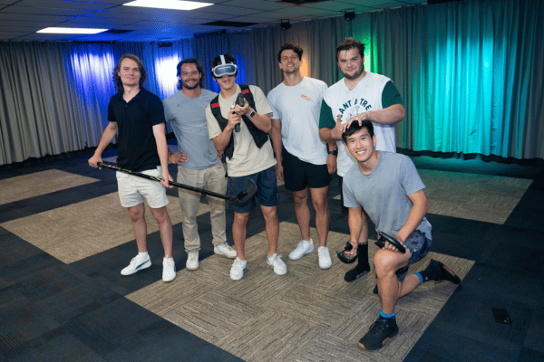 Group of young men, one man wearing a VR headset, one man holding an ice hockey stick