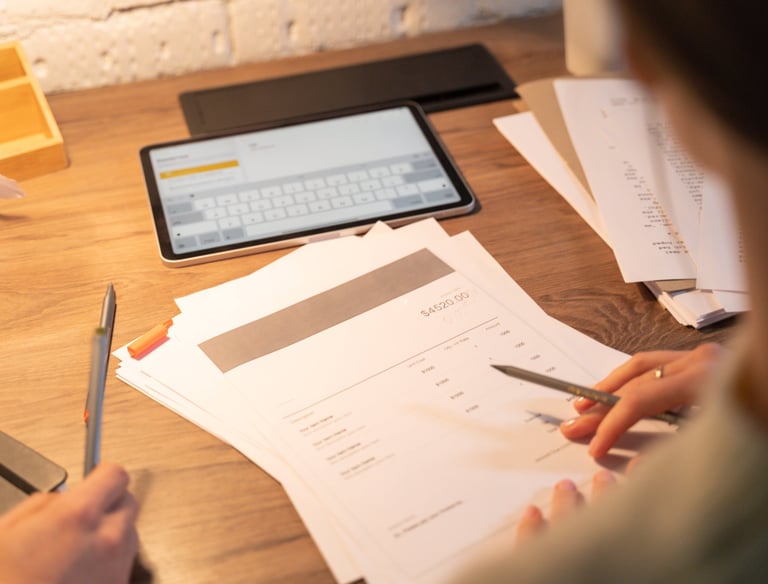 imagem de folhas com descrções de itens, tablet ao fundo e mãos de um homem trabalhando e fazendo anaotações, sobre mesa