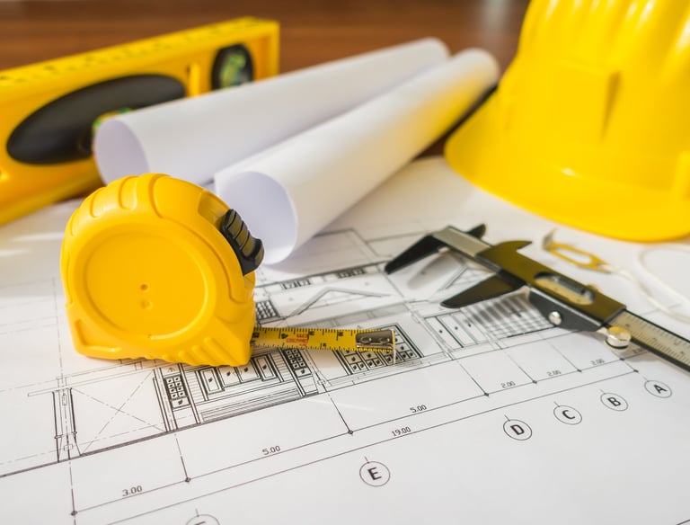 imagem com equipamentos de auxilio em vistorias: trena, capacete, nível e ao fundo uma planta em papel de arquitetura