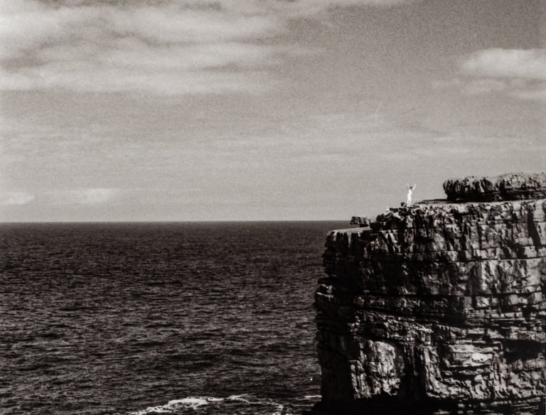 a celebrating figure in the distance, at the top of a peak surrounded by water