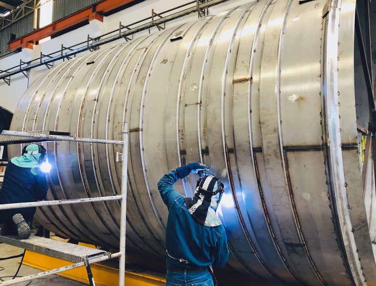 a man welding a large metal pipe in a factory