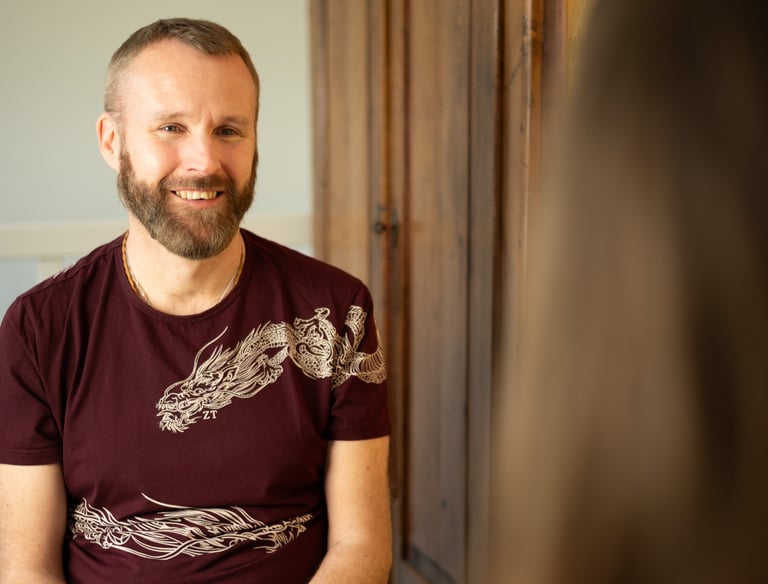 A man wearing a dark red t shirt with dragon imagery is sitting coaching a client