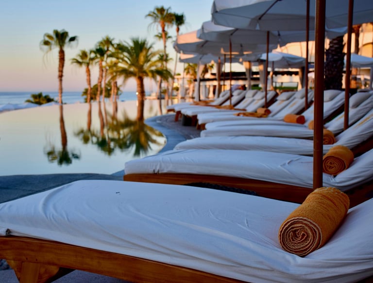 Luxury poolside loungers with umbrellas overlooking palm trees and the ocean.
