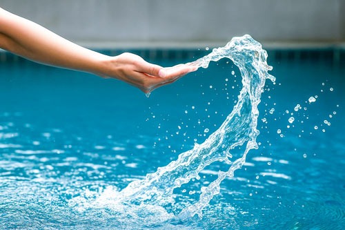 Hand forming a heart with water over a clear pool, symbolizing trusted and caring local pool maintenance services.