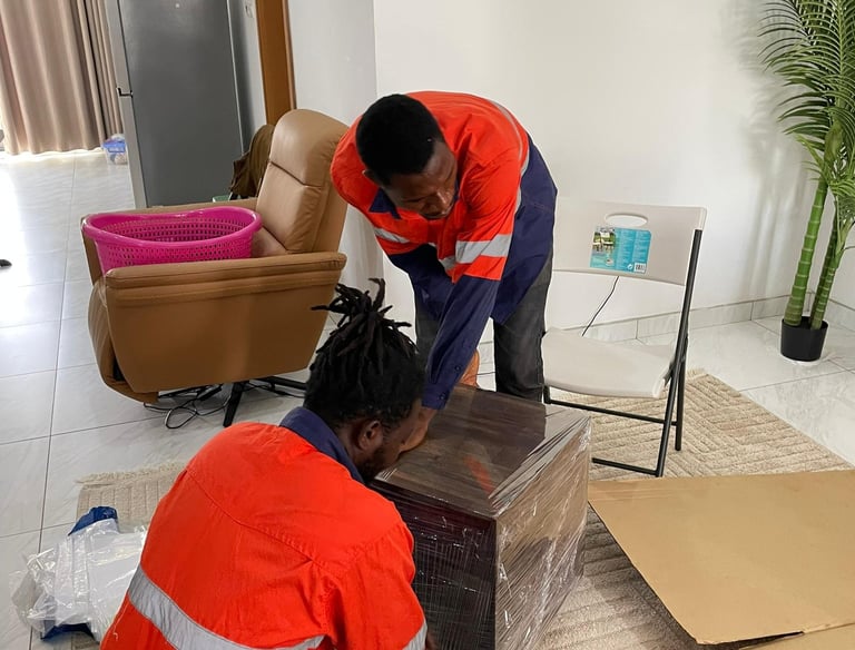 Two professional movers in orange high-visibility vests with reflective stripes collaborate to wrap 