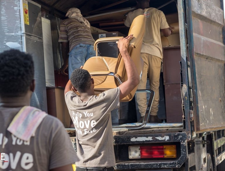 Three professional movers from TE Transporter Express team up to load a beige leather armchair into 