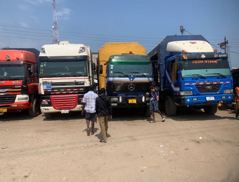 A row of colorful heavy-duty trucks—red MAN, white DAF, yellow flatbed, and blue DAEWOO—parked side 