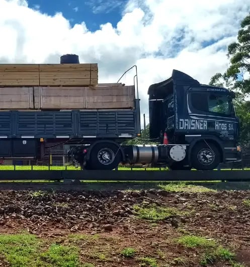 A black Drisner Hnos flatbed semi truck transporting stacks of lumber.
