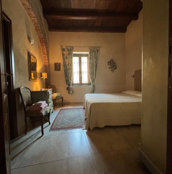 Rustic Tuscan style bedroom featuring a dark wood beamed ceiling, stone archway, and cozy queen bed.