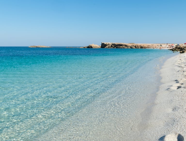 Clear turquoise water and white quartz pebbles at Is Arutas beach in Sardinia under a blue sky.
