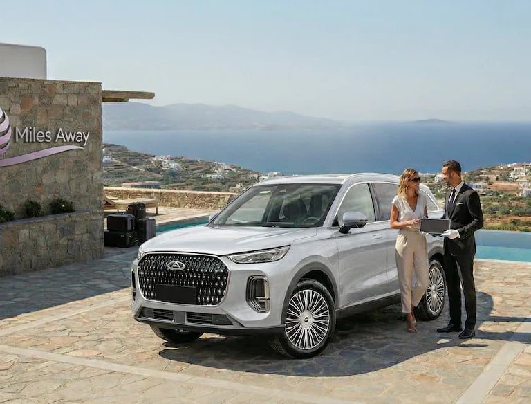 Luxury white Chery SUV parked at a seaside villa with a chauffeur assisting a traveler.