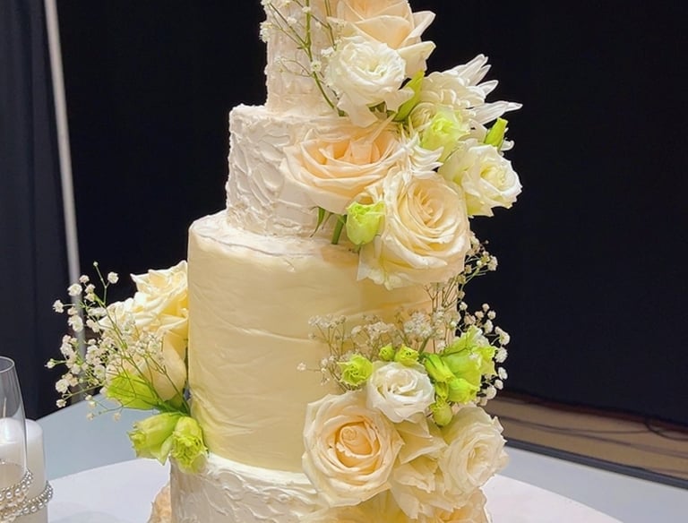 Elegant four-tier white wedding cake decorated with fresh peach roses and baby's breath.