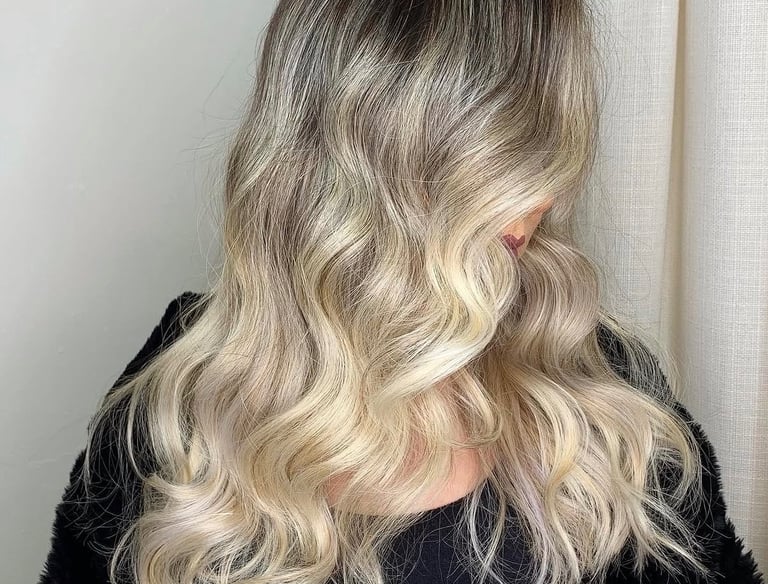 A woman with wavy ash blonde balayage hair featuring dark roots and beach waves.