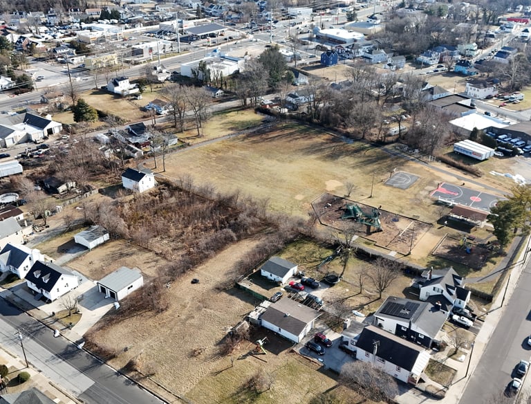 Aerial drone view of a vacant infill lot surrounded by a residential neighborhood and nearby park.