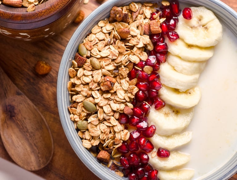 Bowl topped with crunchy granola, fresh pomegranate seeds, sliced bananas & milk