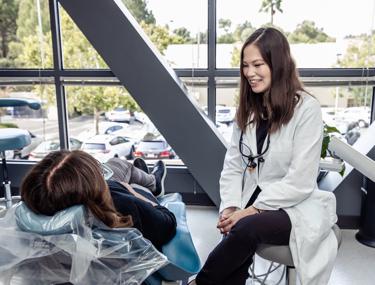 A dentist, Dr. Oyama, smiling as she consults with a patient reclining in a dental chair.